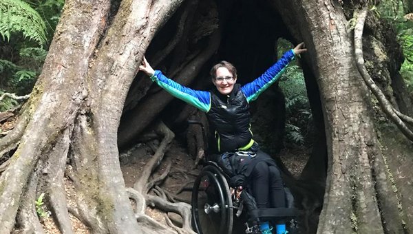 Sonja Häsler sitzt im Rollstuhl im Hohlraum des Stamms eines riesigen Baums