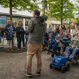 Ein Mann erzählt Rollstuhlfahrern und Menschen ohne Rollstuhl etwas Lustiges