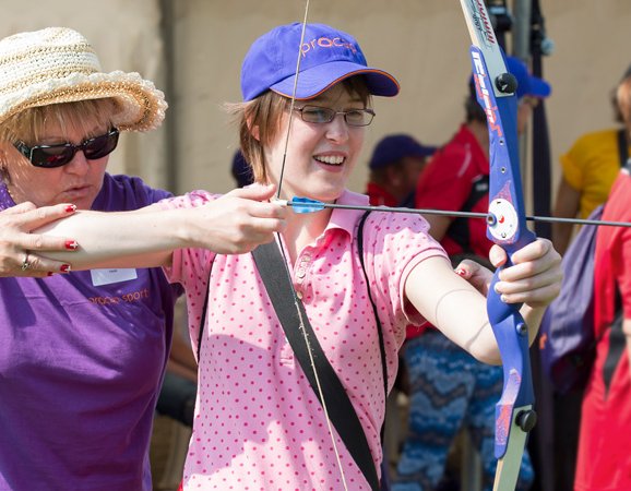 Eine Frau mit Behinderung beim Bogenschiessen, andere Frau unterstützt sie